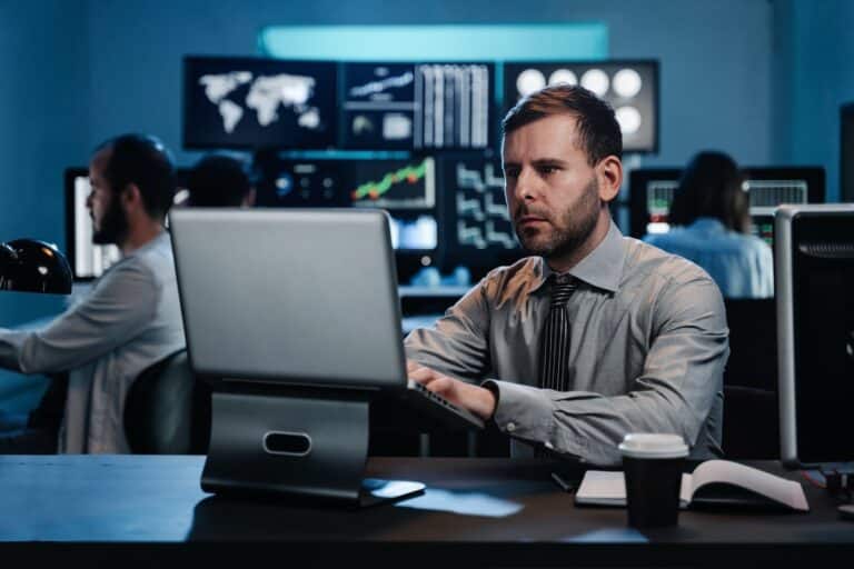 Male trader sitting at desk at office working on laptop