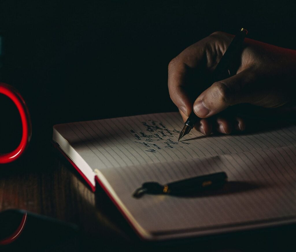 A person writing down in a notebook with a pen