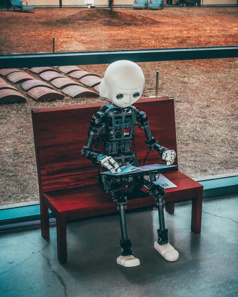 A robot sat on the bench looking at a book
