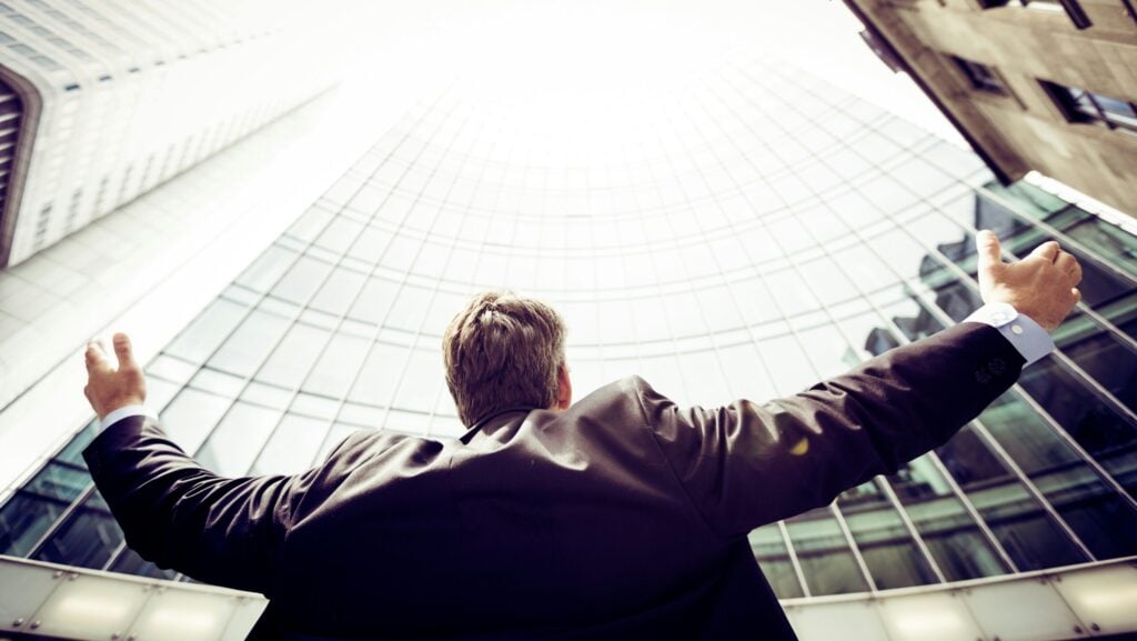 A man celebrating whilst looking up at high buildings in a city