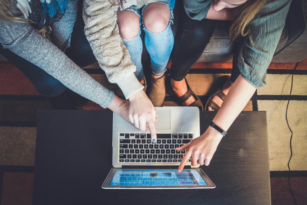 Three people pointing whilst looking at a laptop screen on a table